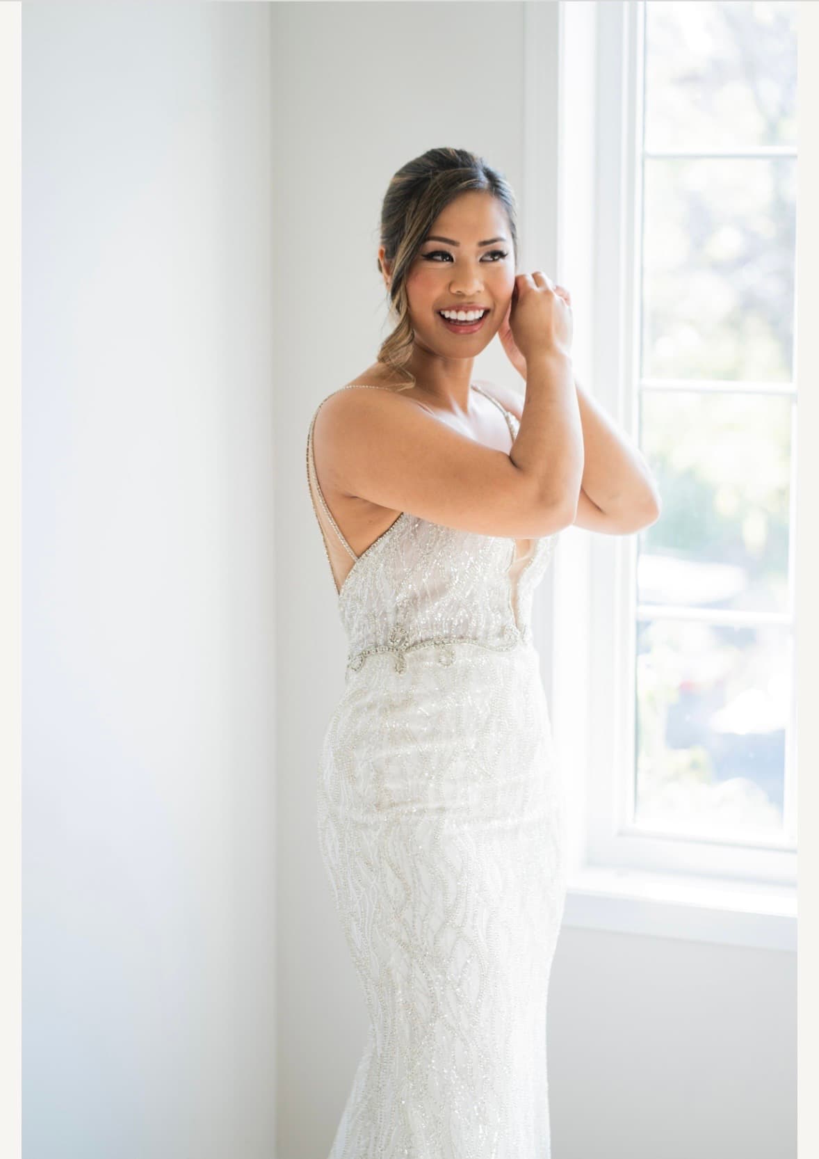 Bride putting on earring by window with dramatic natural light