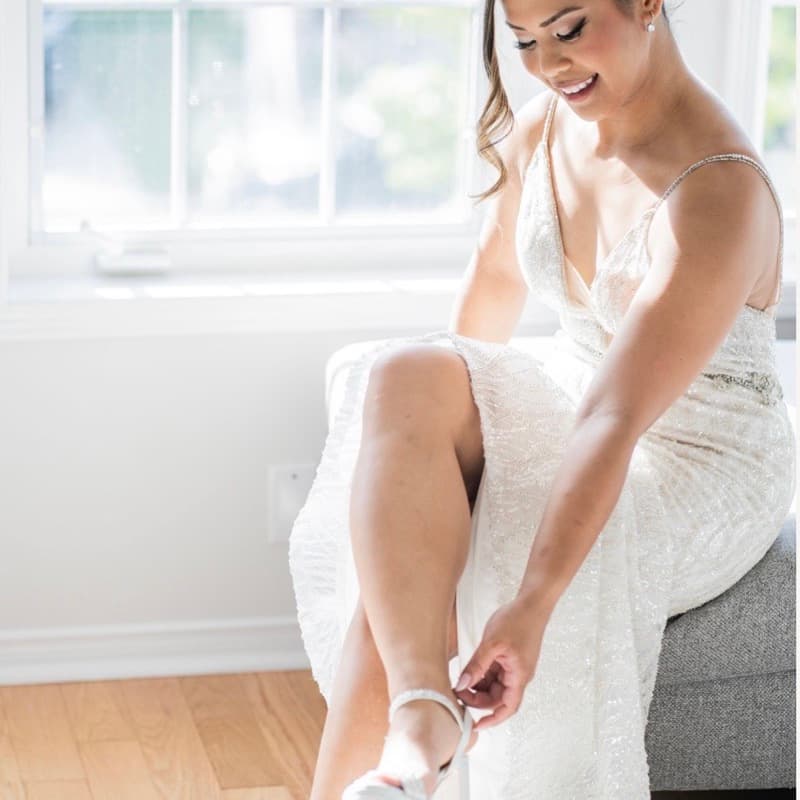 Bride fastening her shoe by the window on wedding morning
