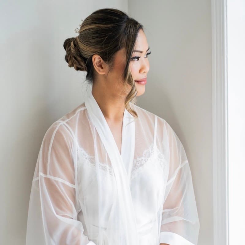 Bride in sheer robe with soft glam makeup looking out the window