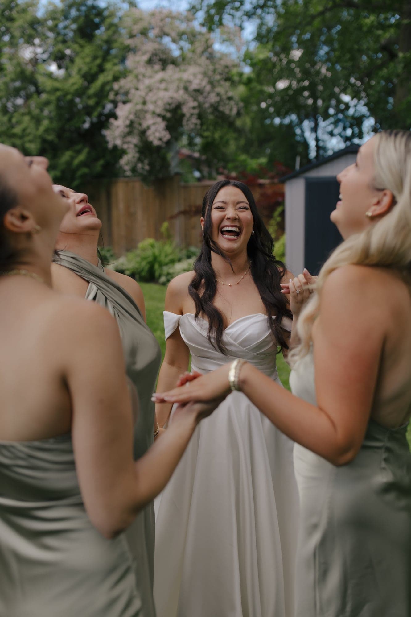 Bride laughing outdoors with her bridesmaids in sage dresses after getting ready